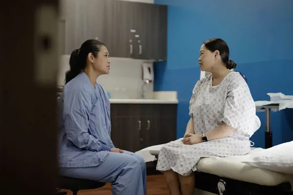 Patient in a hospital gown in an exam room speaking with her doctor.