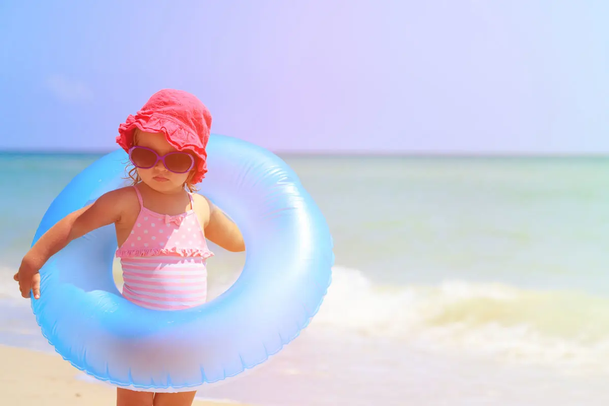 A child holding a flotation device at the beach with the surf in the background.