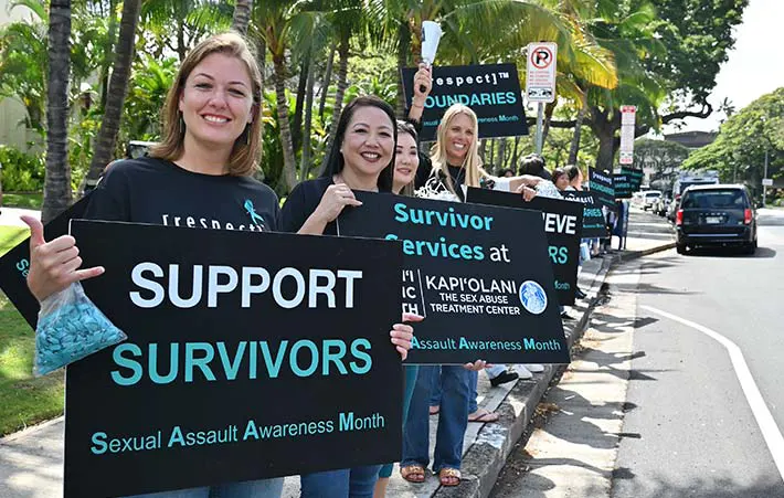 People wearing denim and waving signs on the side of the road in support of Sexual Assault Awareness Month and Denim Day.