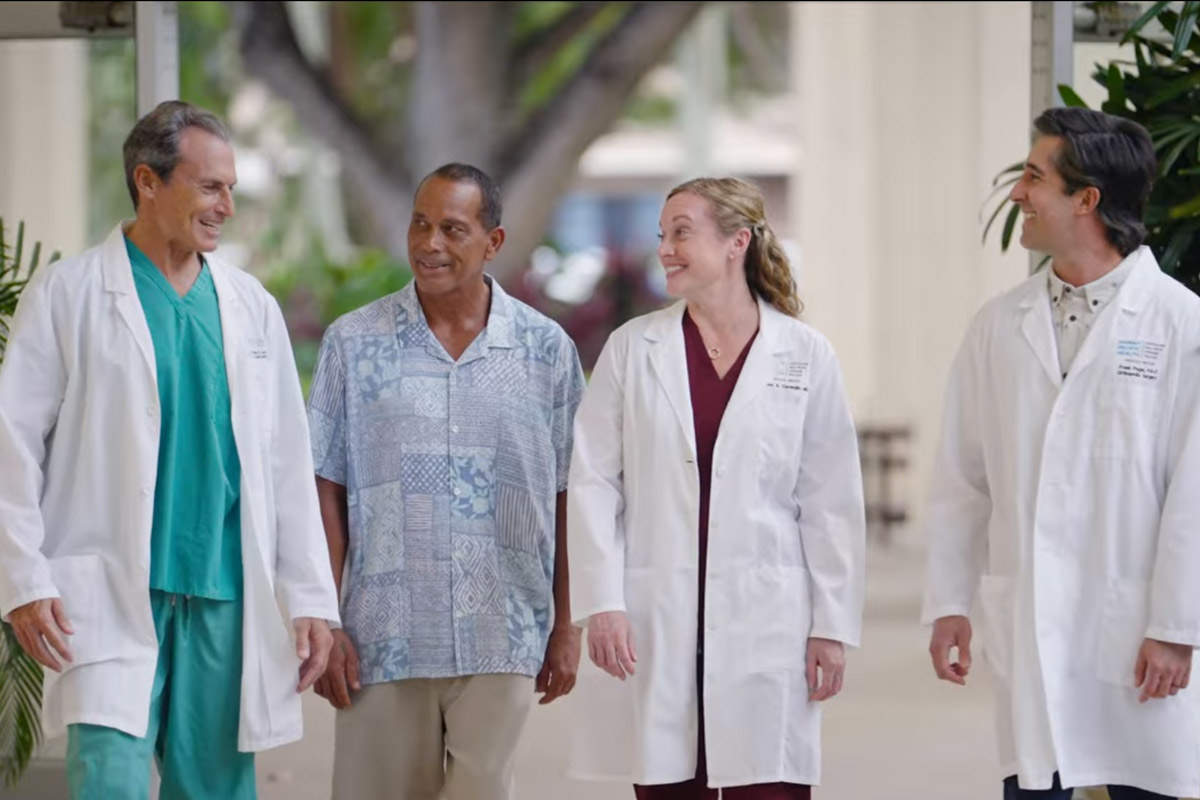 Man in aloha shirt walks alongside three doctors in white coats. 