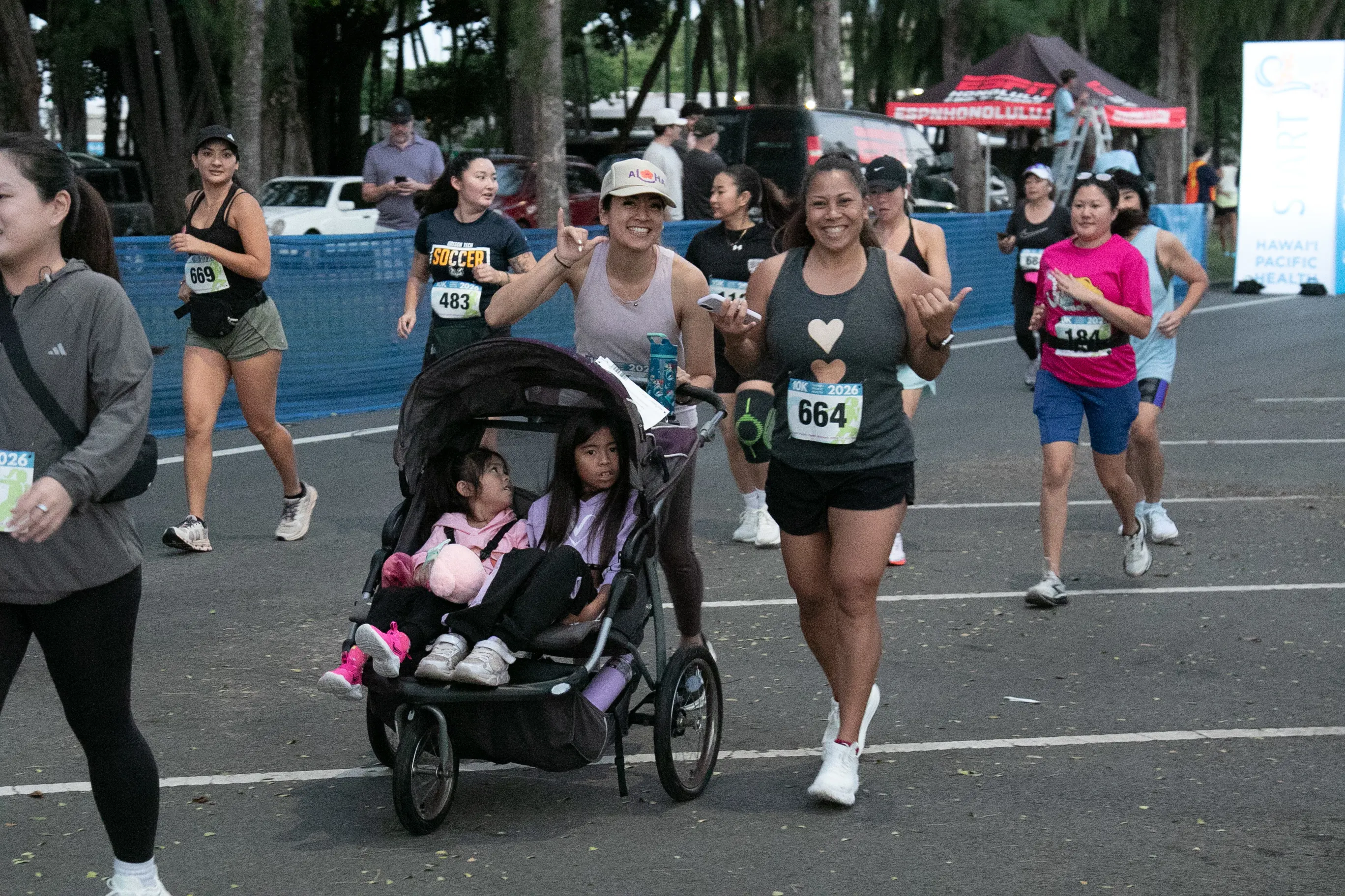 Woman smiling as she starts the 10K race while pushing a stroller with two kids in it.
