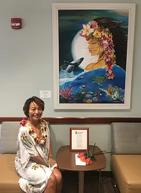 Woman smiling in front of an abstract painting of the ocean at night, which she created. 