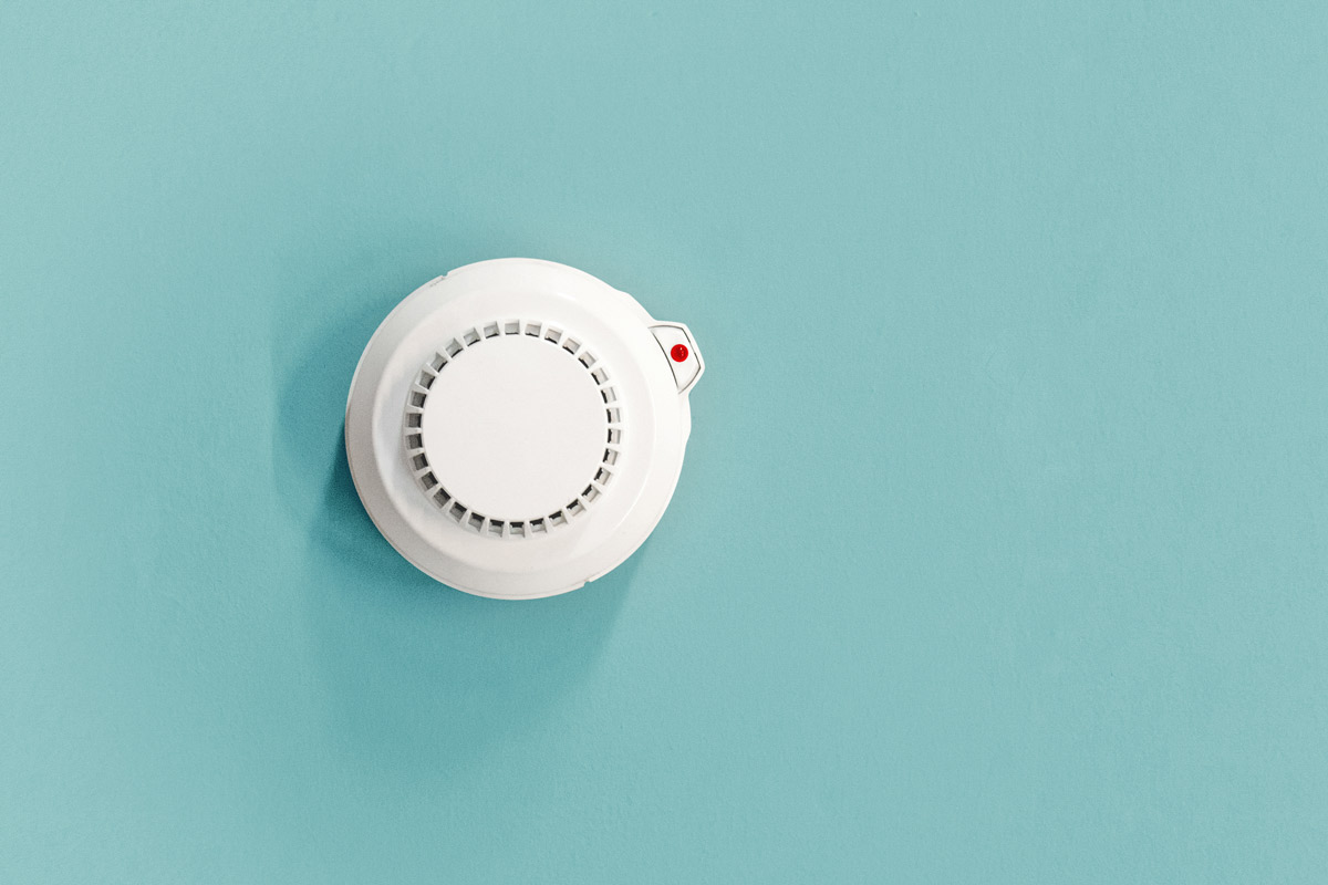An overhead view of a smoke detector mounted on a teal ceiling.