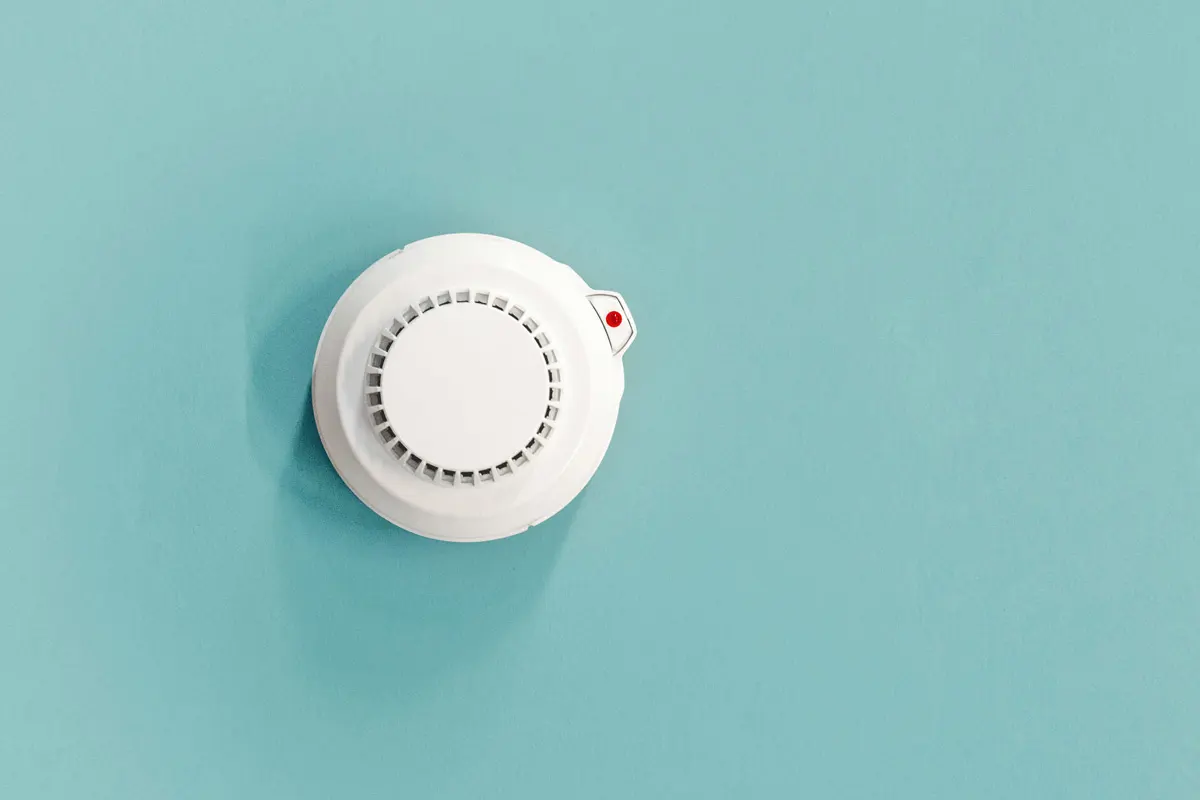 An overhead view of a smoke detector mounted on a teal ceiling.