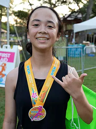 Race finisher wearing a pink and orange medal smiling and holding up a shaka.