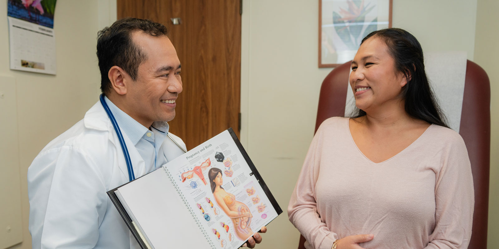an ob-gyn shows a medical diagram to a patient who is pregnant in an exam room
