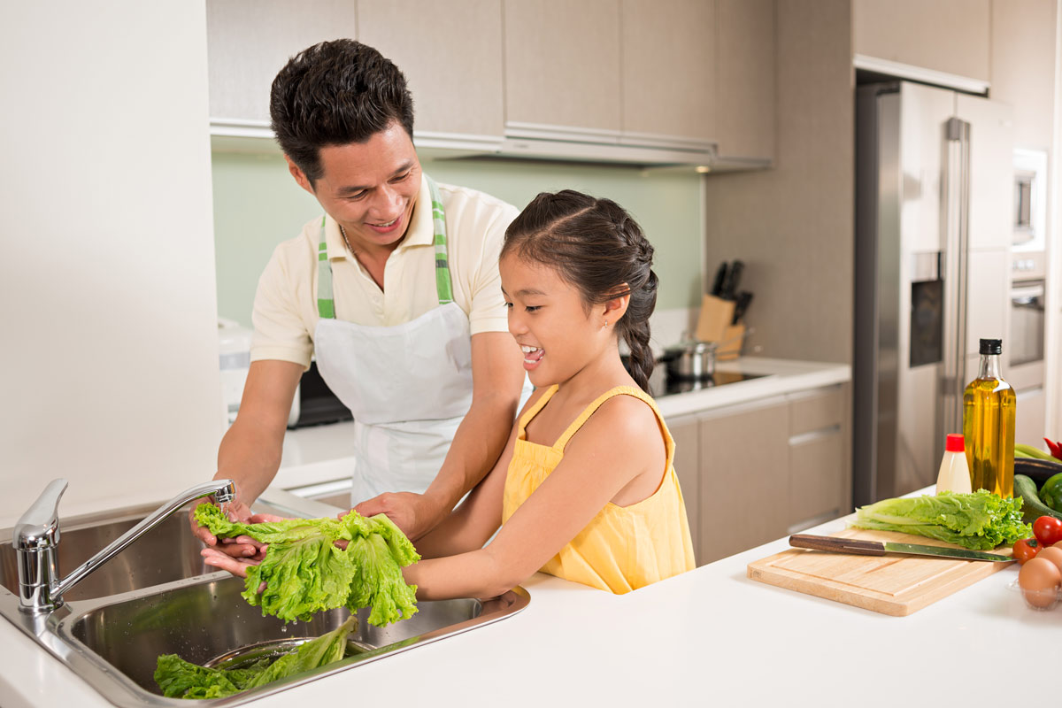 A father and daughter washing lettuce.