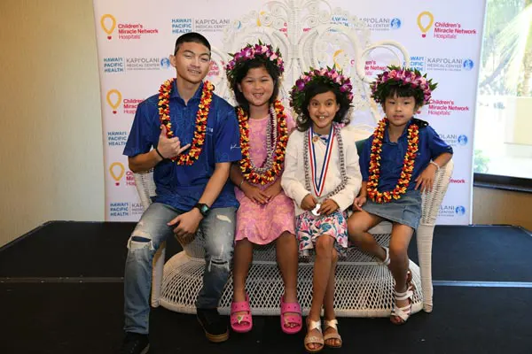 Aurelia Awa smiling with three previous Hawaii CMN Champions, wearing lei, and sitting on a bench.