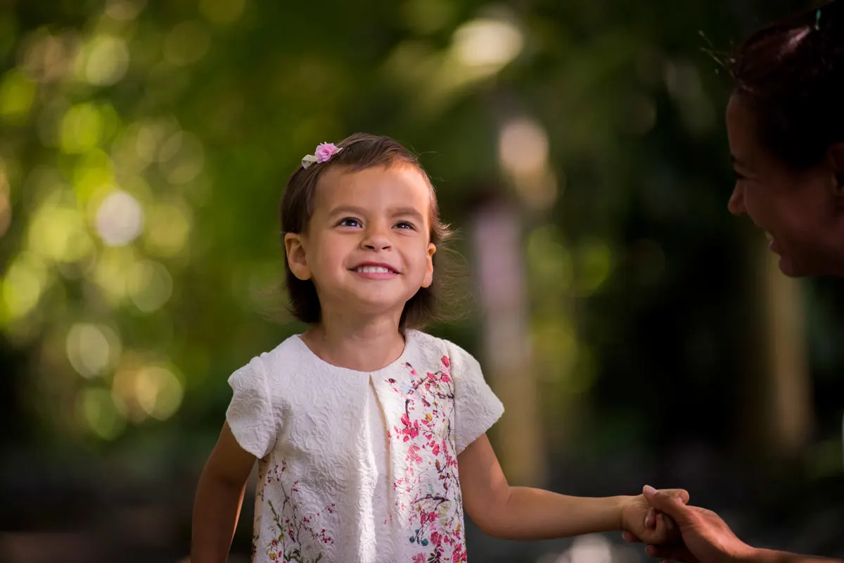 young girl wearing a white floral printed dress smiling while her mom holds her hand.