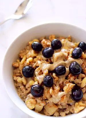 Blueberries sit on top of a bowl of cauliflower "oats" in a white bowl.