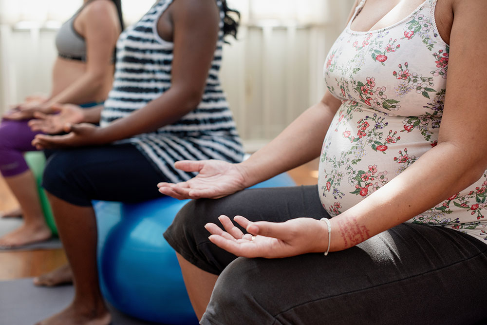 Pregnant women seated on exercise balls will hands on knees facing up. 