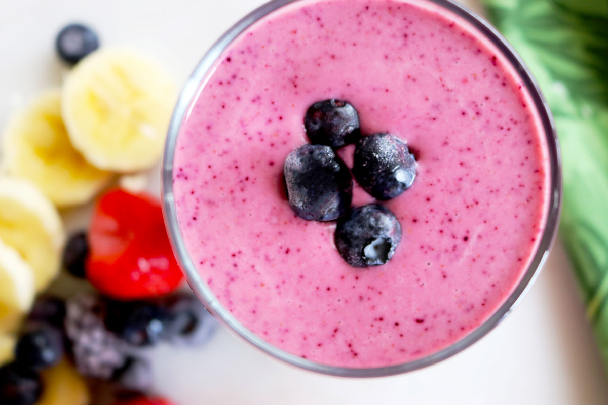 A glass of Banana Berry Blast Smoothie sits on a counter with fruit and a tropical-print napkin