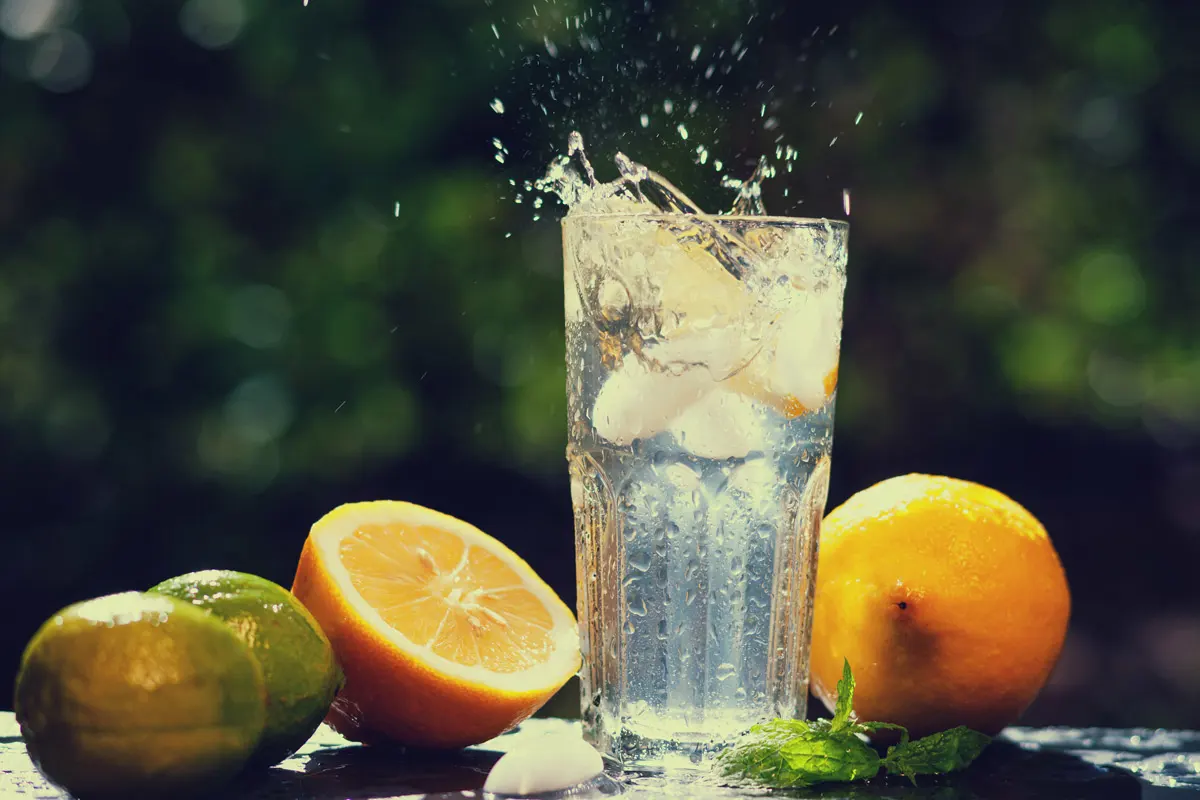 Ice splashes into a glass of water surrounded by citrus fruit.