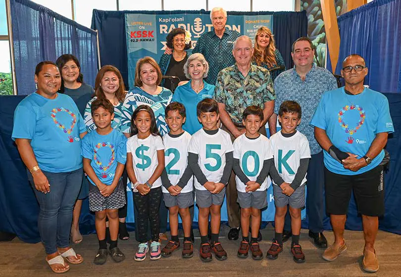 Group of kids wearing tshirts that spell out $250K standing in front of the KSSK Radiothon booth.