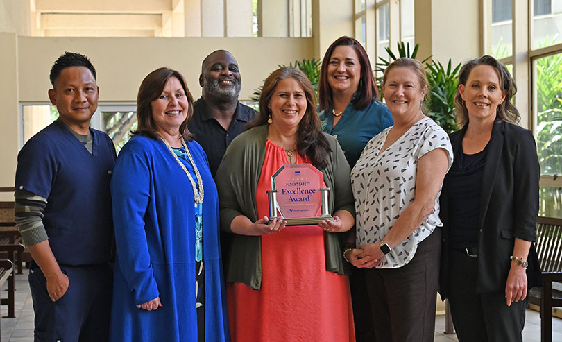 Group of people gathered in the Wilcox lobby smiling and posing with an award for patient safety.