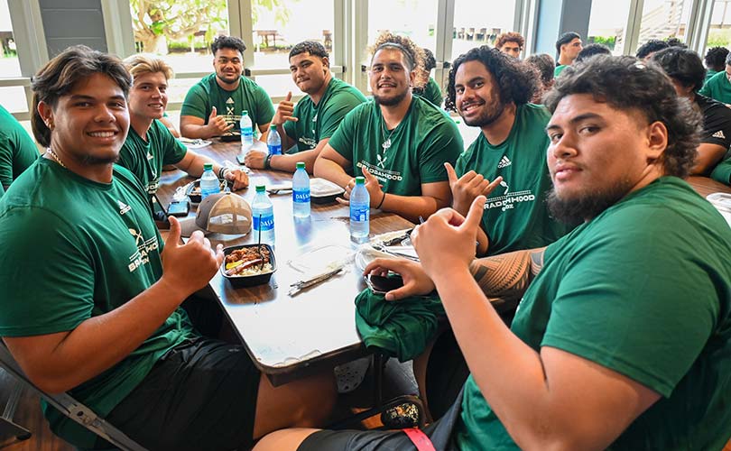 Players from the Rainbow Warrior football team gathered at a table, smiling, and enjoying lunch.
