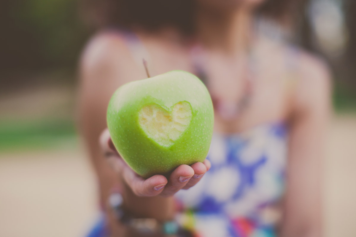 Woman holding an apple with a heart-shaped bite taken out of it.