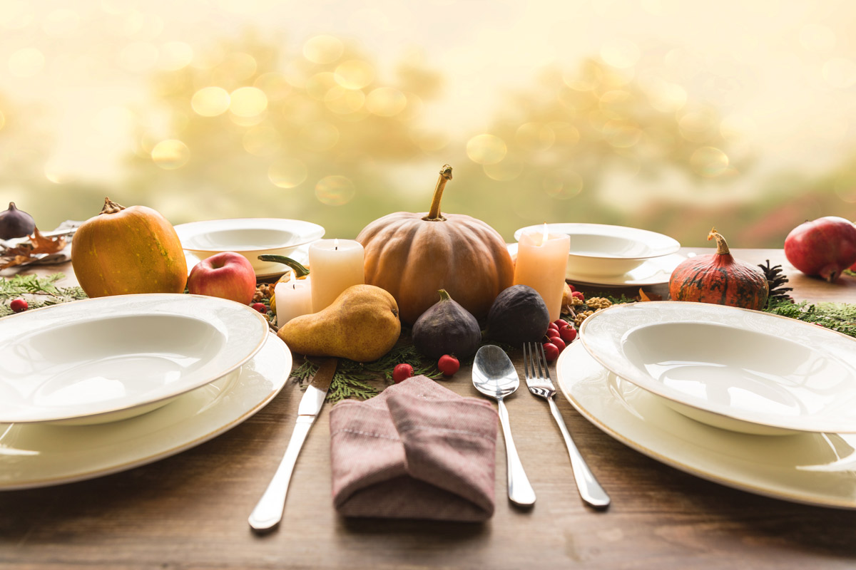 Four plates with cutlery and autumnal vegetables on wooden table.