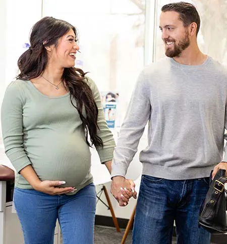 Young expecting couple smiling at each other and holding hands while walking.
