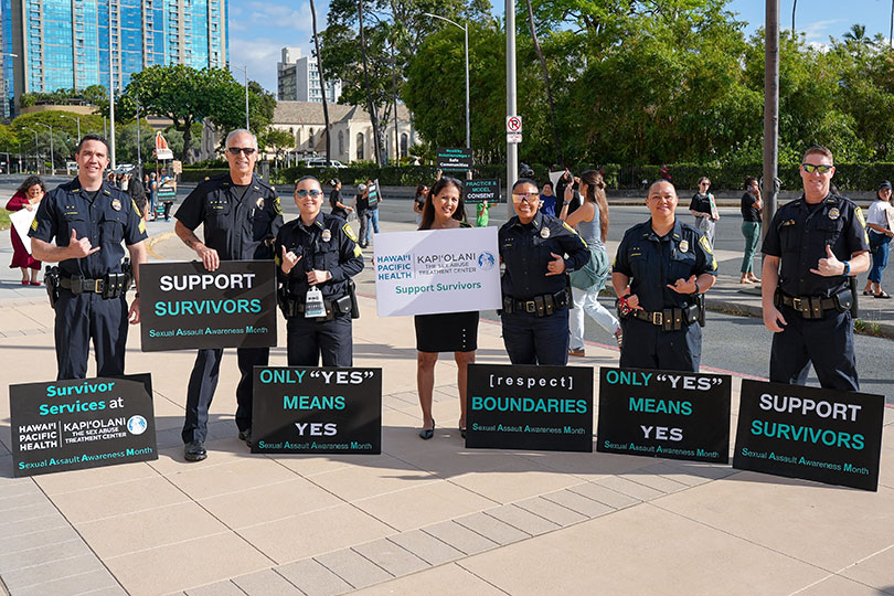 Group of police officers smiling with signs in support of Sexual Assault Awareness month.
