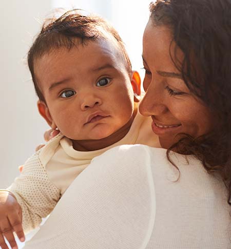 Curious baby looking at the camera while being held by young woman.
