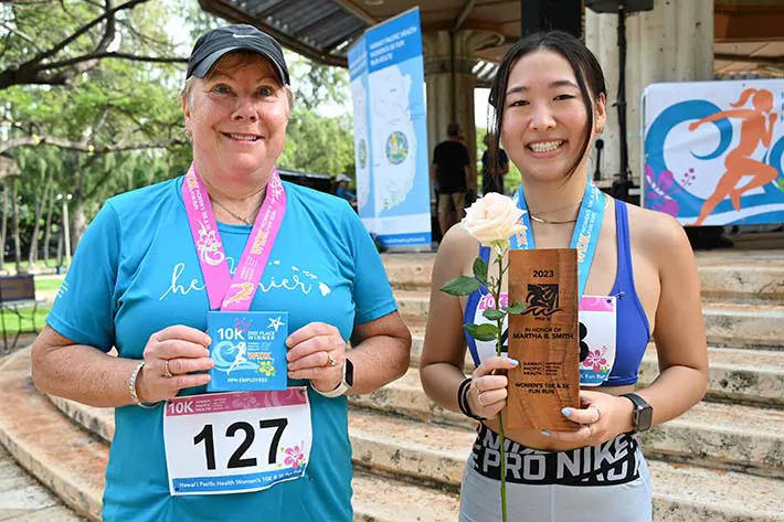 Two race finishers smiling and holding up their medals and awards.