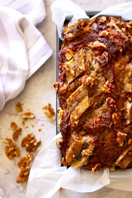 A top-down view of a rustic loaf with large chunks of banana and walnut.