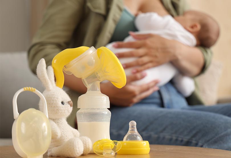 Mom breastfeeding baby with manual pump and bottle with breast milk nearby.