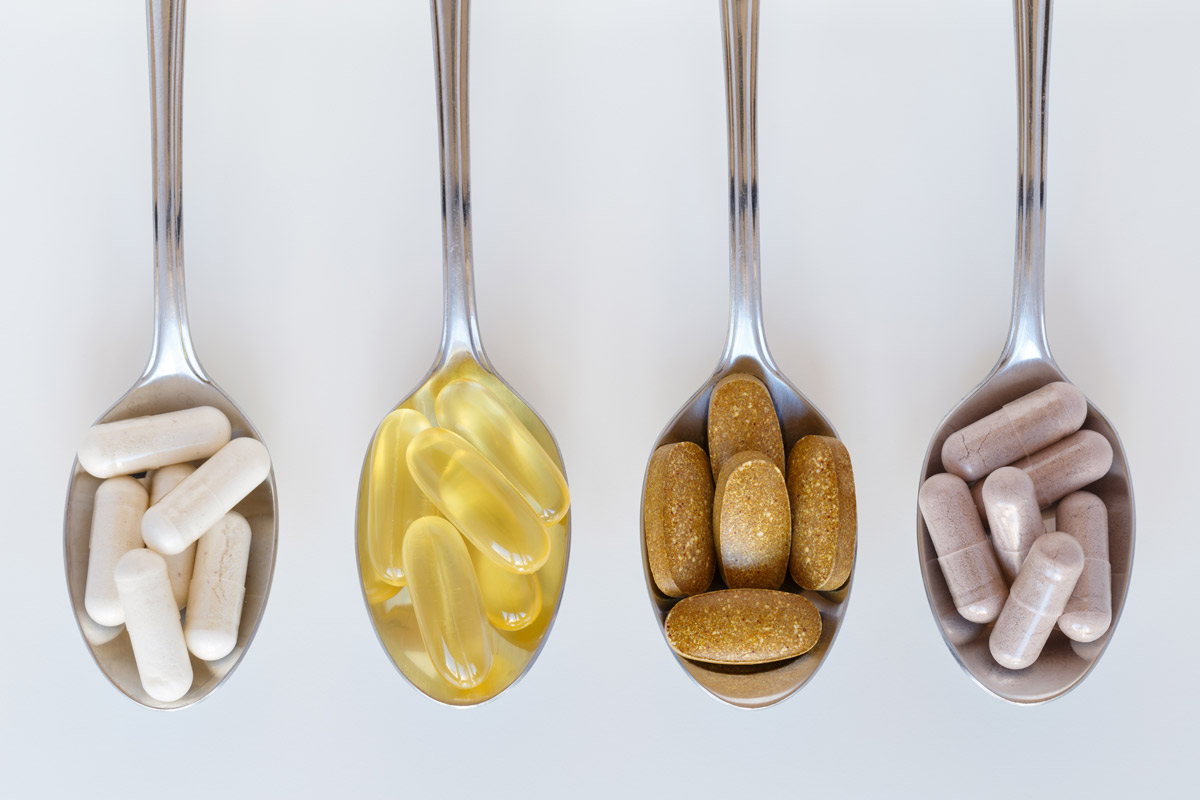 Four spoons containing different vitamin and supplements pills set up in a line on a counter.