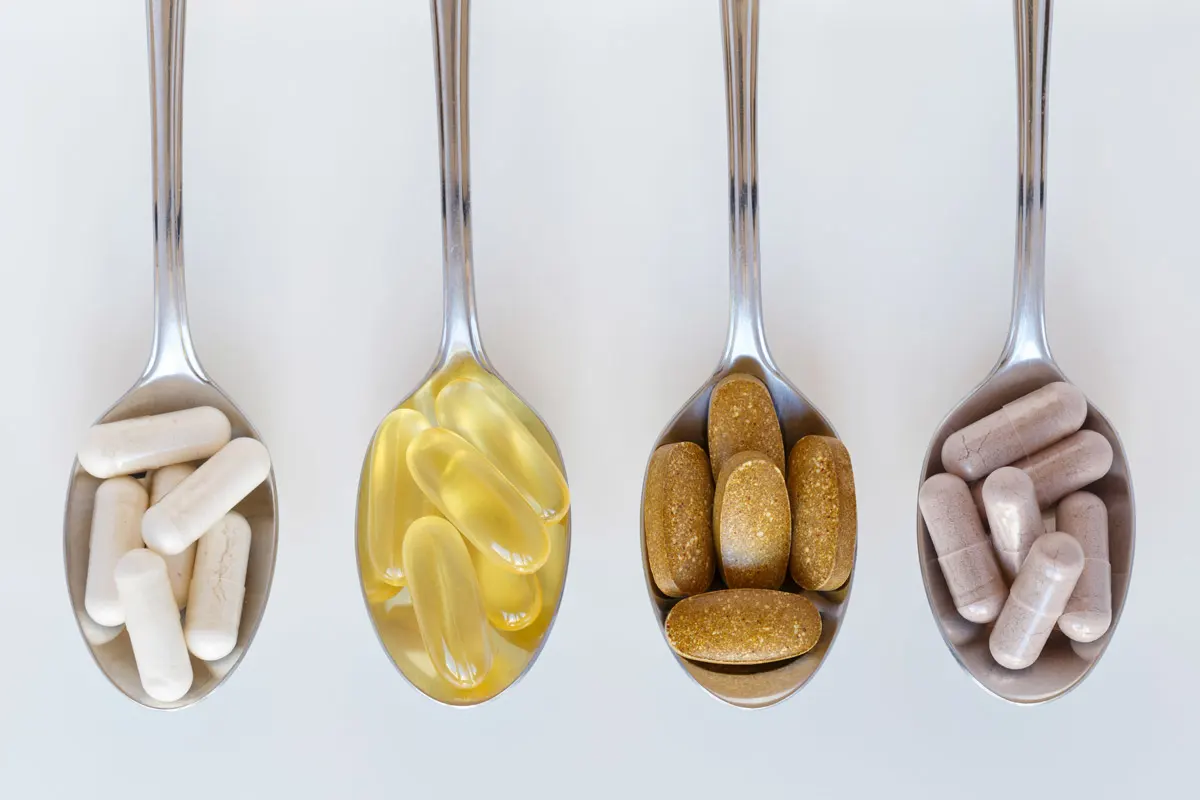 Four spoons containing different vitamin and supplements pills set up in a line on a counter.
