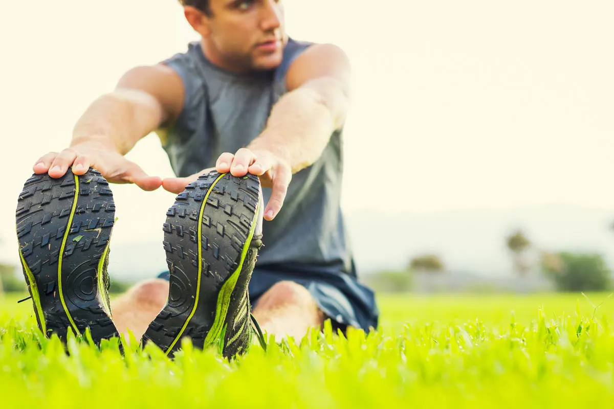 A man sitting in the grass stretching to touch his toes.