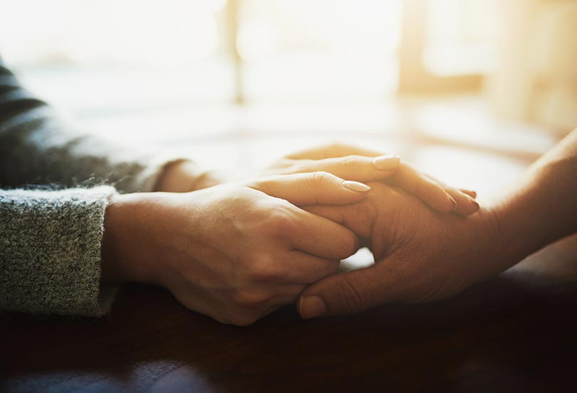 Close up of two people's clasped hands in soft lighting.