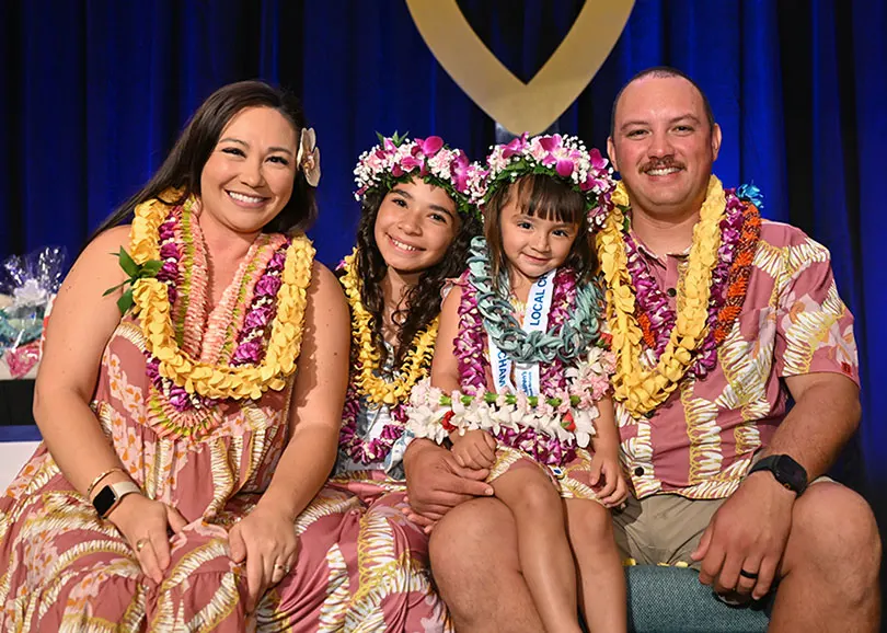 Family of four in matching pink floral outfits adorned with lei. 