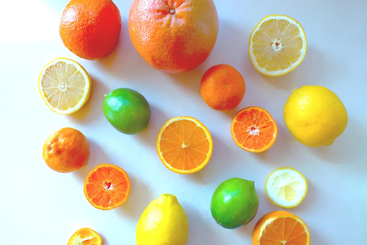 Whole and sliced citrus arranged on a white background, including lemons, grapefruit, and oranges and limes.
