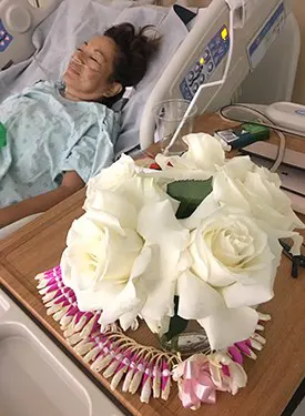White floral arrangement and orchid lei next to a female patient resting in the hospital.