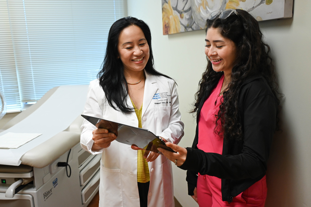 female physician speaking with female patient as they look at a chart.