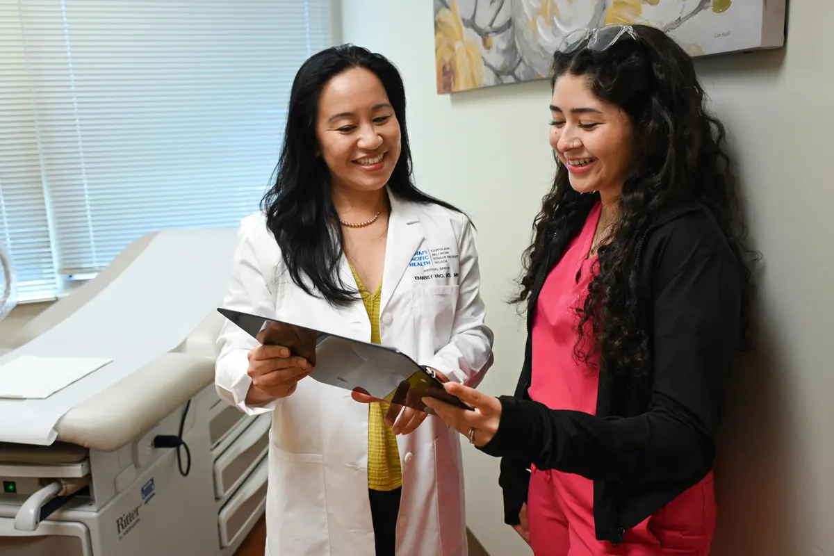 female physician speaking with female patient as they look at a chart.