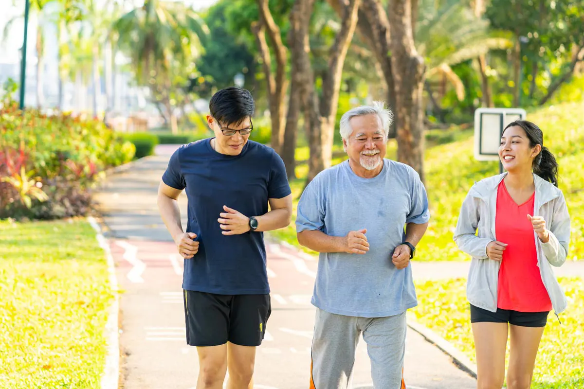 an older adult man runs on a paved beachside path with his adult son and daughter.