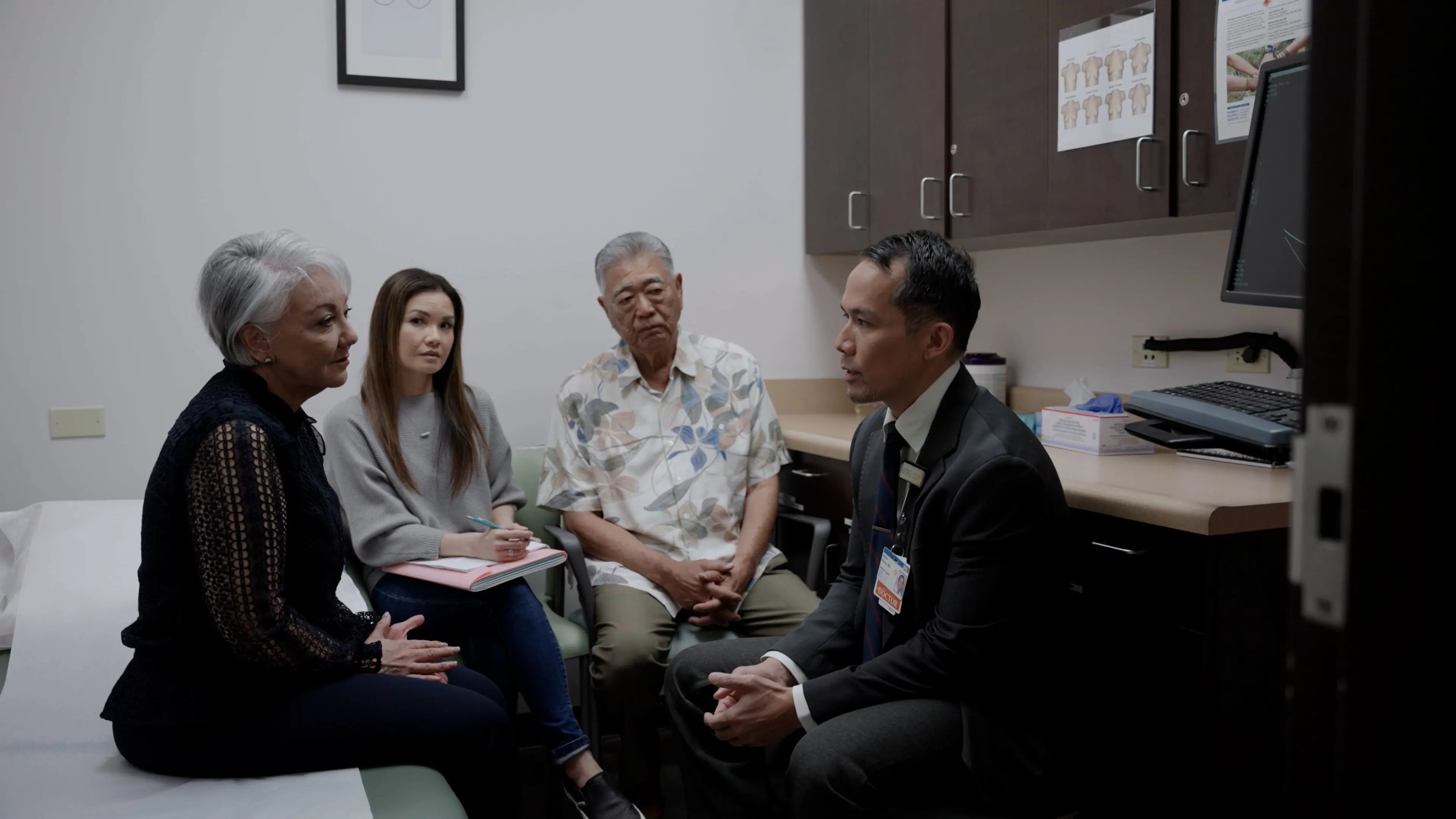 Male doctor having a serious conversation with his patient and her loved ones in a consultation room.